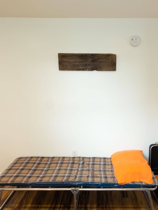 Fold-out cot with plaid bedding and an orange pillow