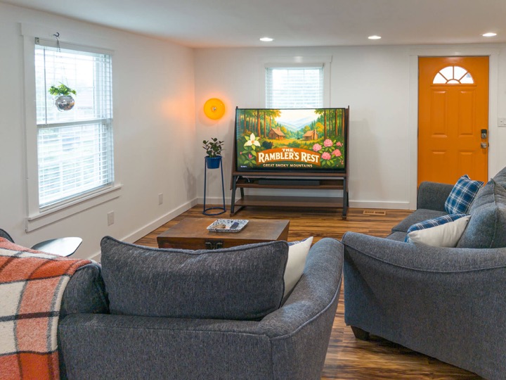 Living room with gray seating, an art TV, and an orange front door